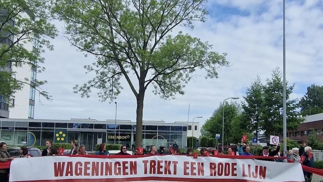 Rij met mensen die achter een banner staan waarop staat ‘Wageningen trekt een rode lijn’.