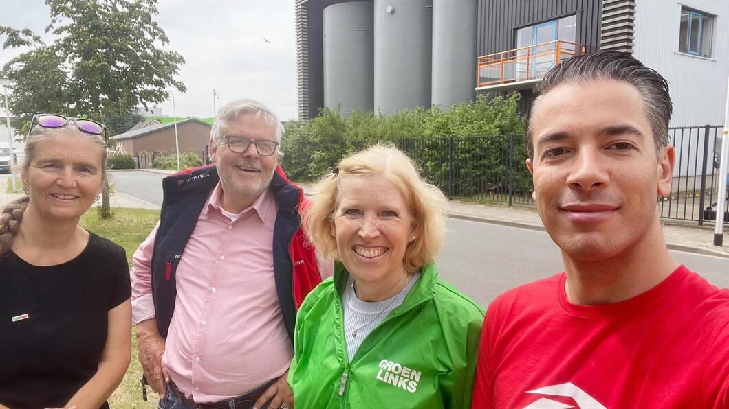 4 mensen in rood en groene kleding, leden van GroenLinks-PvdA, staan voor de biomassacentrale in Ede.