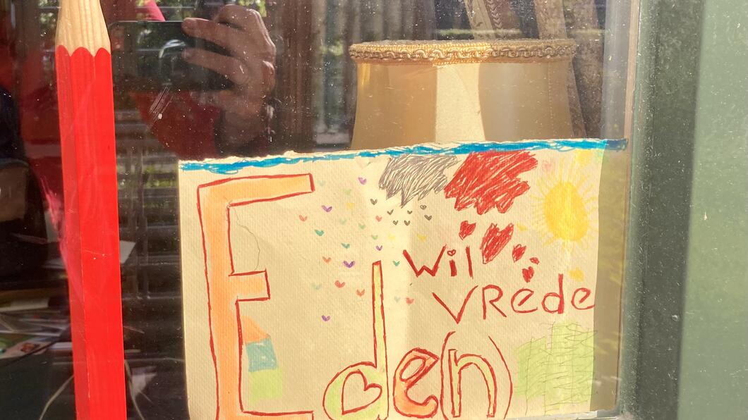 Groot rood potlood en papier ernaast met tekst ‘Ede(n) wil vrede’.
