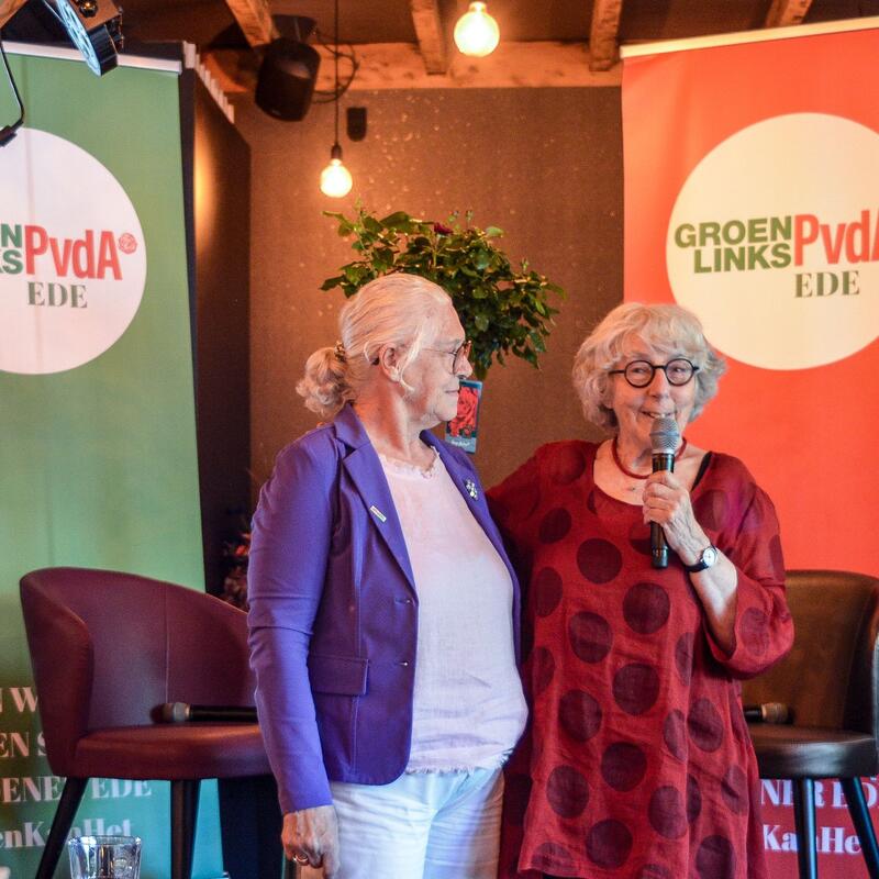 Voor een groene en rode GroenLinks-PvdA banner staan 2 vrouwen, Betty Mijlof en Liesbeth van Dijk.