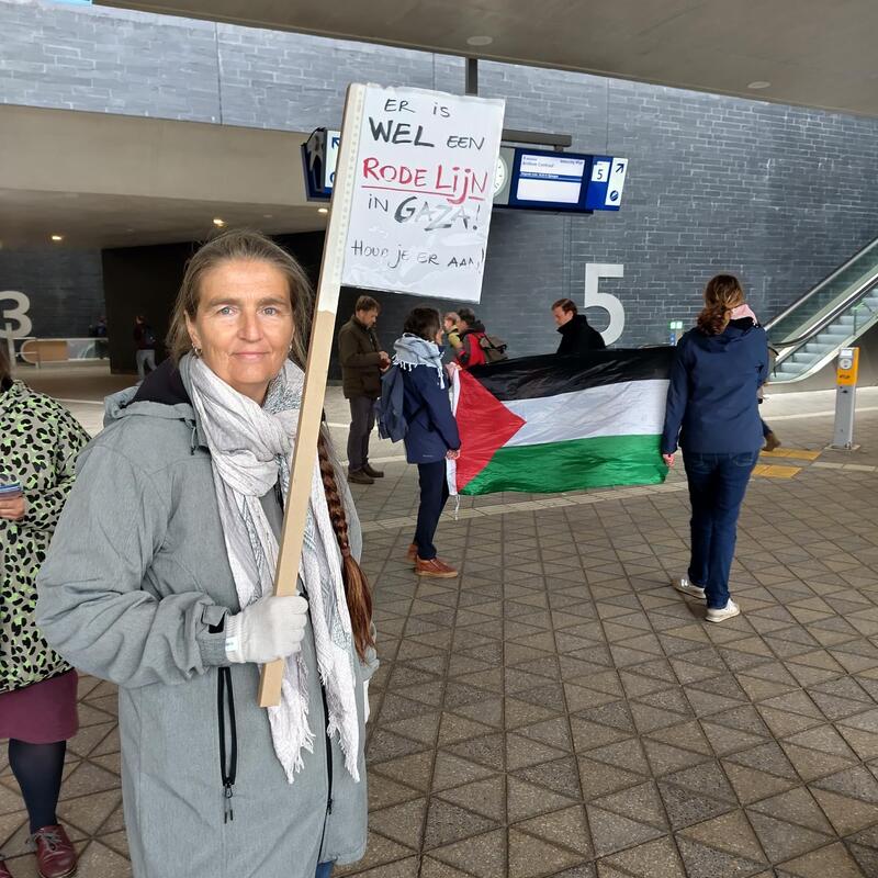 Vrouw in lange grijze jas (onze fractievolger Tita) houd een protestbord omhoog ‘er is wel een rode lijn, hou je eraan!’