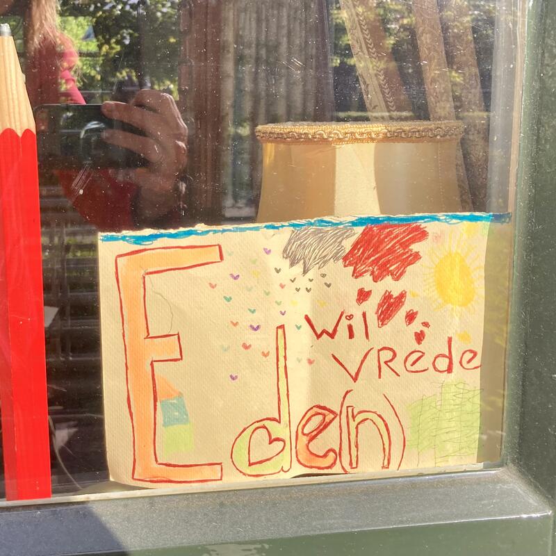 Groot rood potlood en papier ernaast met tekst ‘Ede(n) wil vrede’.