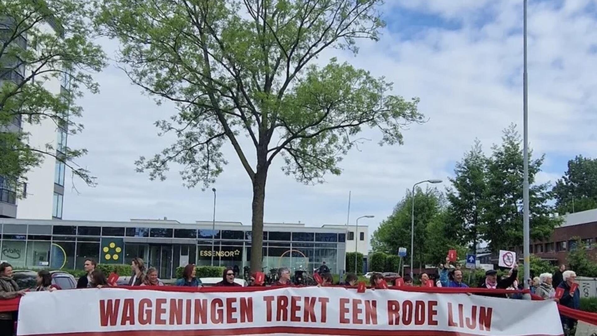 Rij met mensen die achter een banner staan waarop staat ‘Wageningen trekt een rode lijn’.