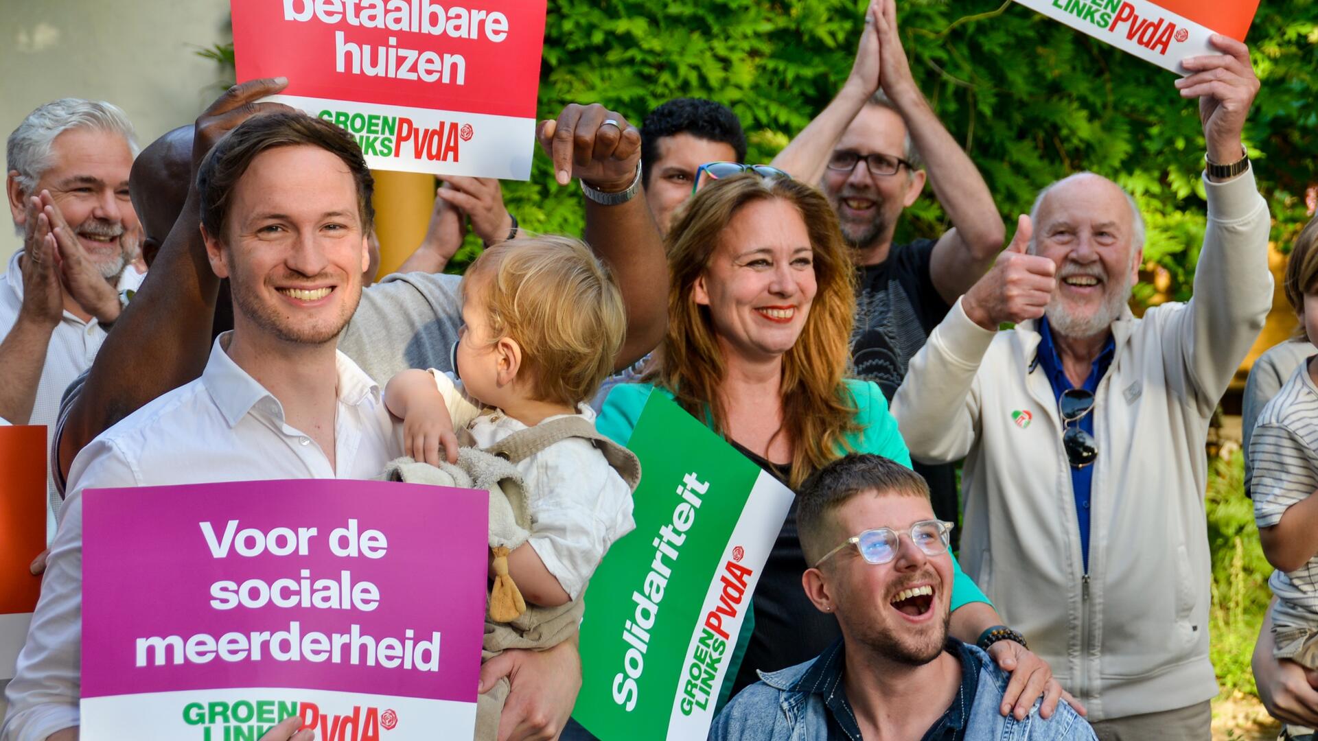 Een groep mensen waarvan de man links vooraan in de camera kijkt, hij houdt een tekstbord vast met de tekst ‘voor de sociale meerderheid’. 
